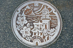 日本海を背景に立つ余部埼灯台と町の花「サツキ」が描かれた汚水用マンホール蓋。